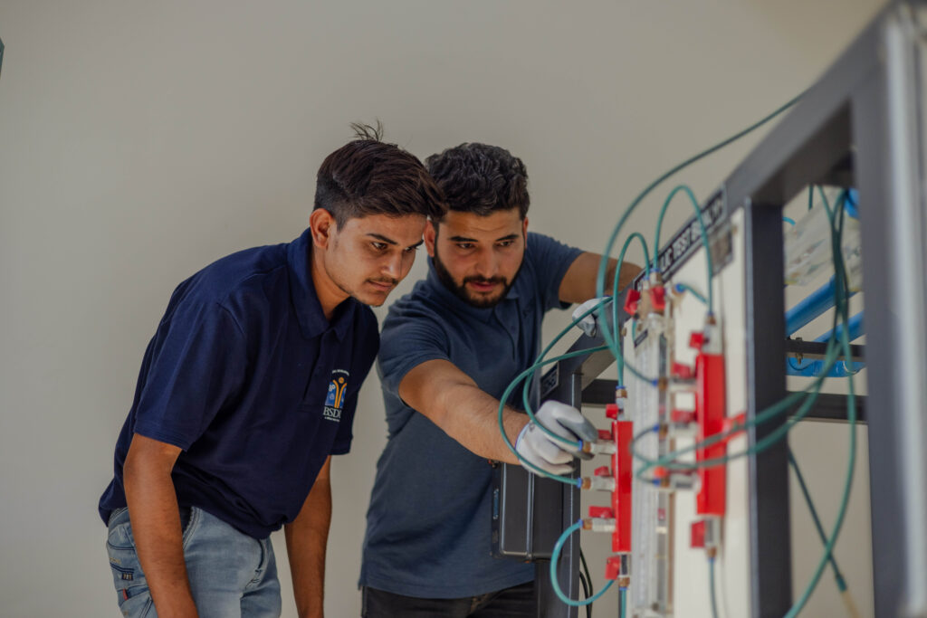 Zwei BSDU-Studenten arbeiten konzentriert an einem technischen Trainingspanel mit Mess- und Verbindungselementen im Labor.